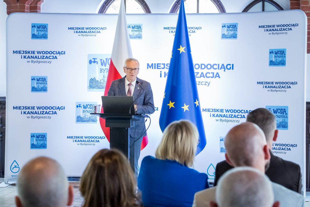 Prezes Miejskich Wodociągów i Kanalizacji w Bydgoszczy na tle unijnych flag
