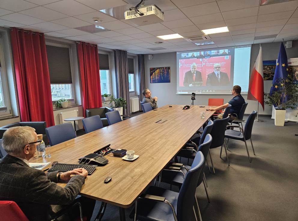 Sala konferencyjna z widokiem na ekran, na którym transmitowana jest konferencja online